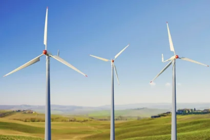 Drei Windkraftanlagen auf einem grünen Feld unter blauem Himmel